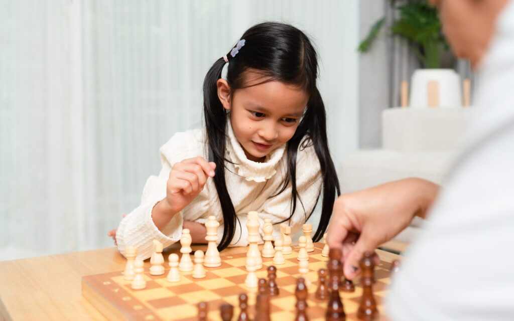 Asian little girl is playing chess board game withe father in the living room with happy moment.