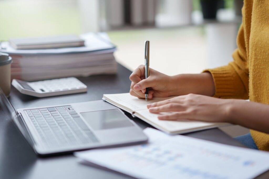 Close-up of a woman intently writing and taking notes in a notebook in the office.