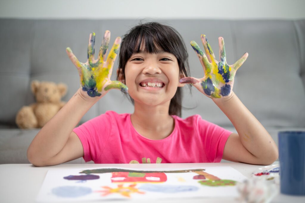 education, school, art and painitng concept - little student girl showing painted hands