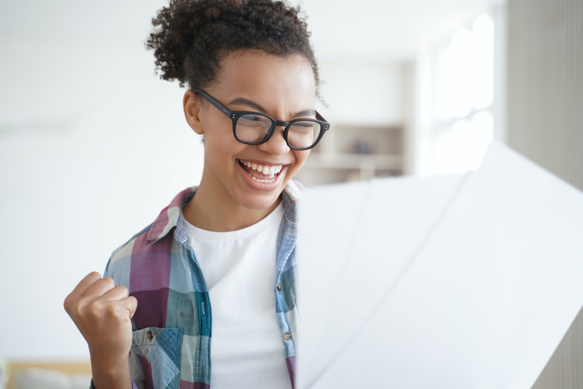 Excited spanish schoolgirl is winner holding letter. Afro teenage girl pupil is accepted to college.