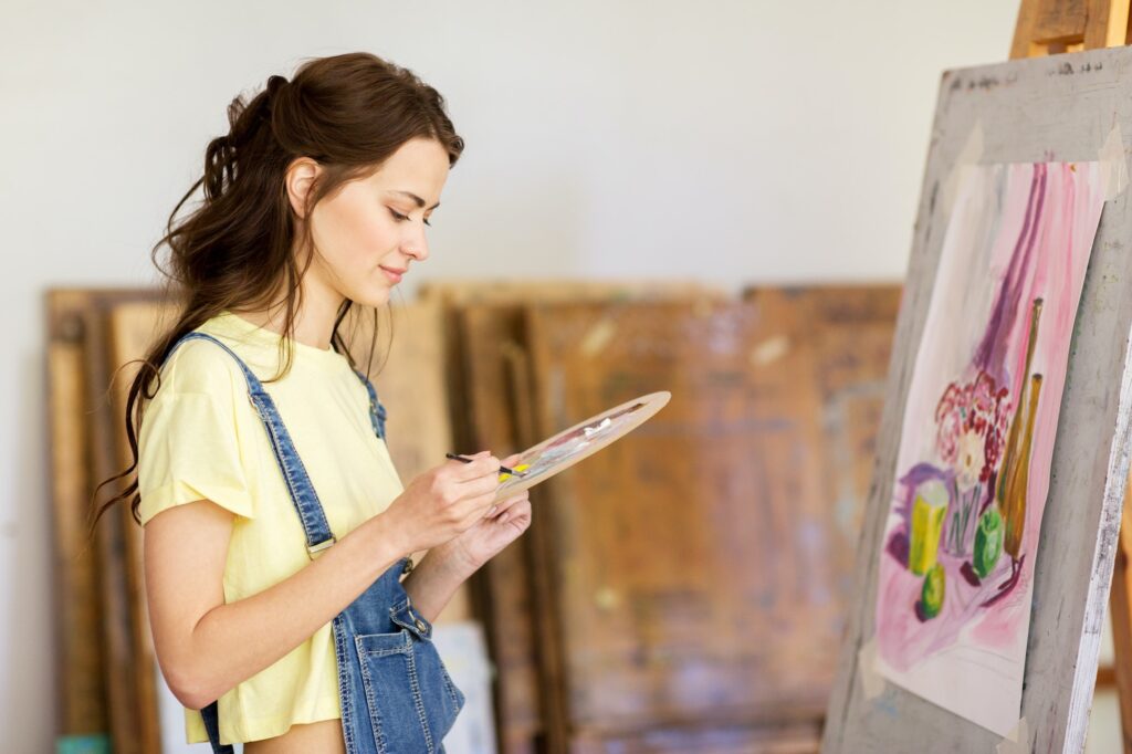 student girl with easel painting at art school