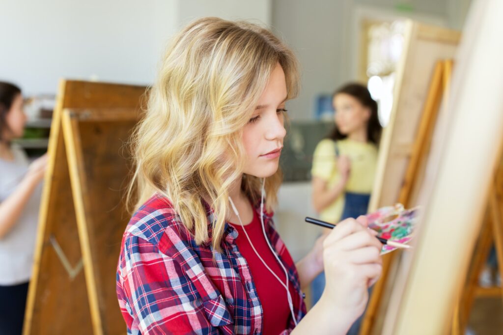 student girl with easel painting at art school