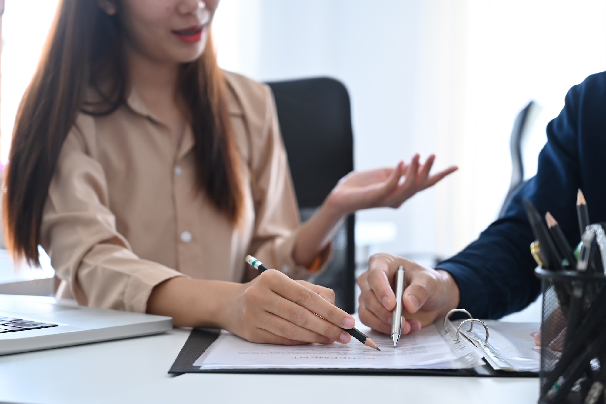 Two young businesspeople reviewing financial documents together at office desk.